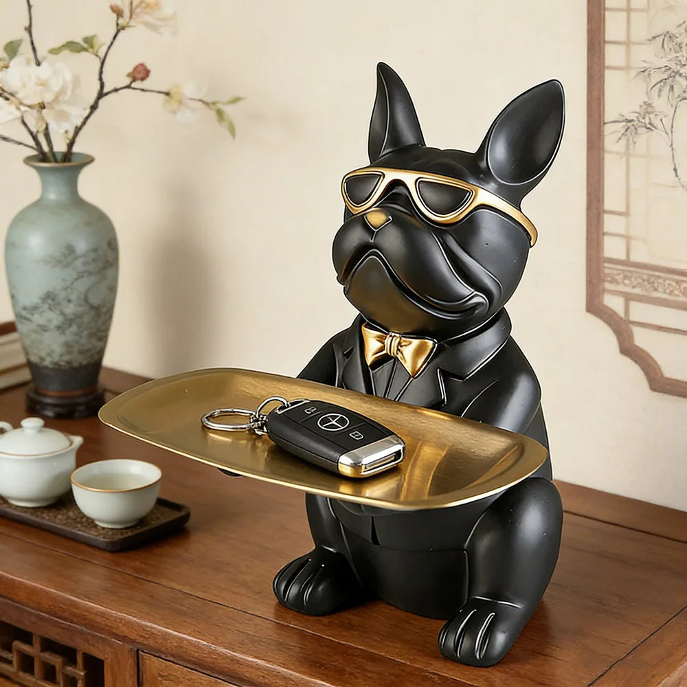 A black decorative bulldog figurine wearing gold sunglasses and holding a leather key on a gold tray.