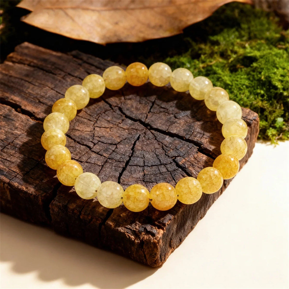 A round bracelet made of yellow citrine crystal beads resting on dark wood next to green moss.