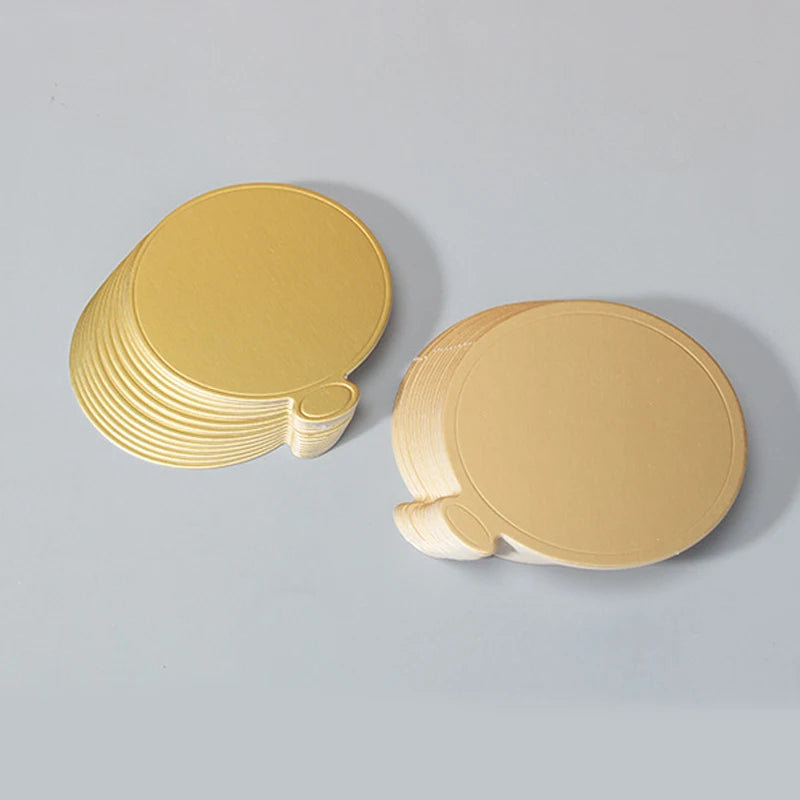 A stack of metallic gold dessert cake boards with silver edges, shown on a light gray surface.