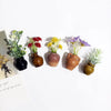 A collection of mini ceramic vases with artificial flowers in various colors like green, red, yellow, and purple.