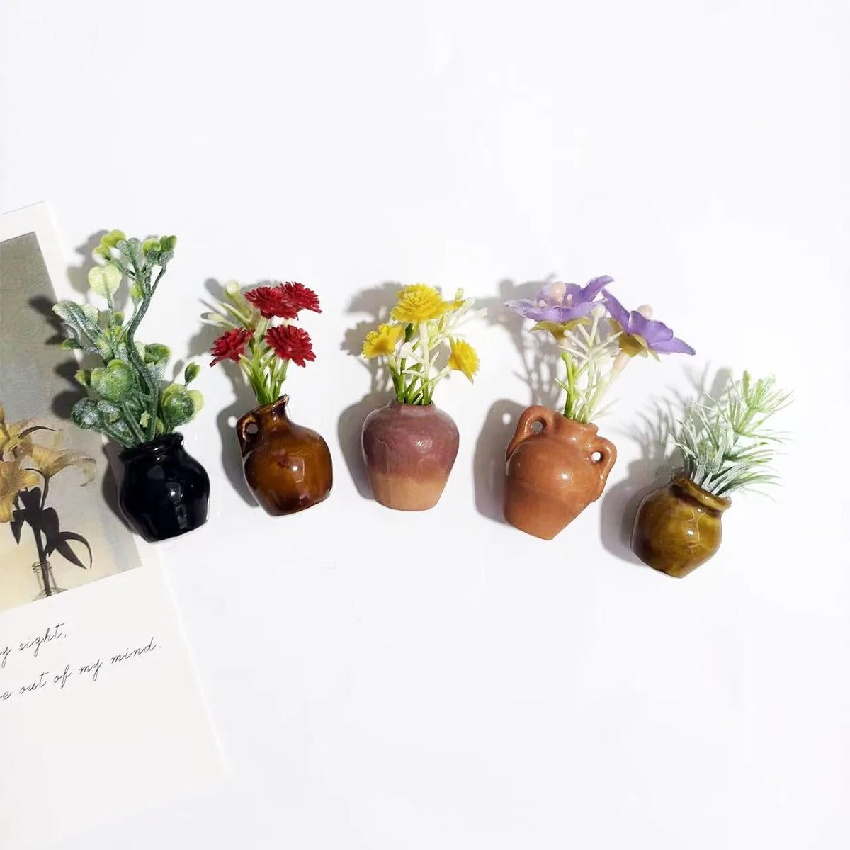 A collection of mini ceramic vases with artificial flowers in various colors like green, red, yellow, and purple.