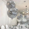 A display of silver disco ball foil balloons in various sizes and a chandelier decoration for a party.