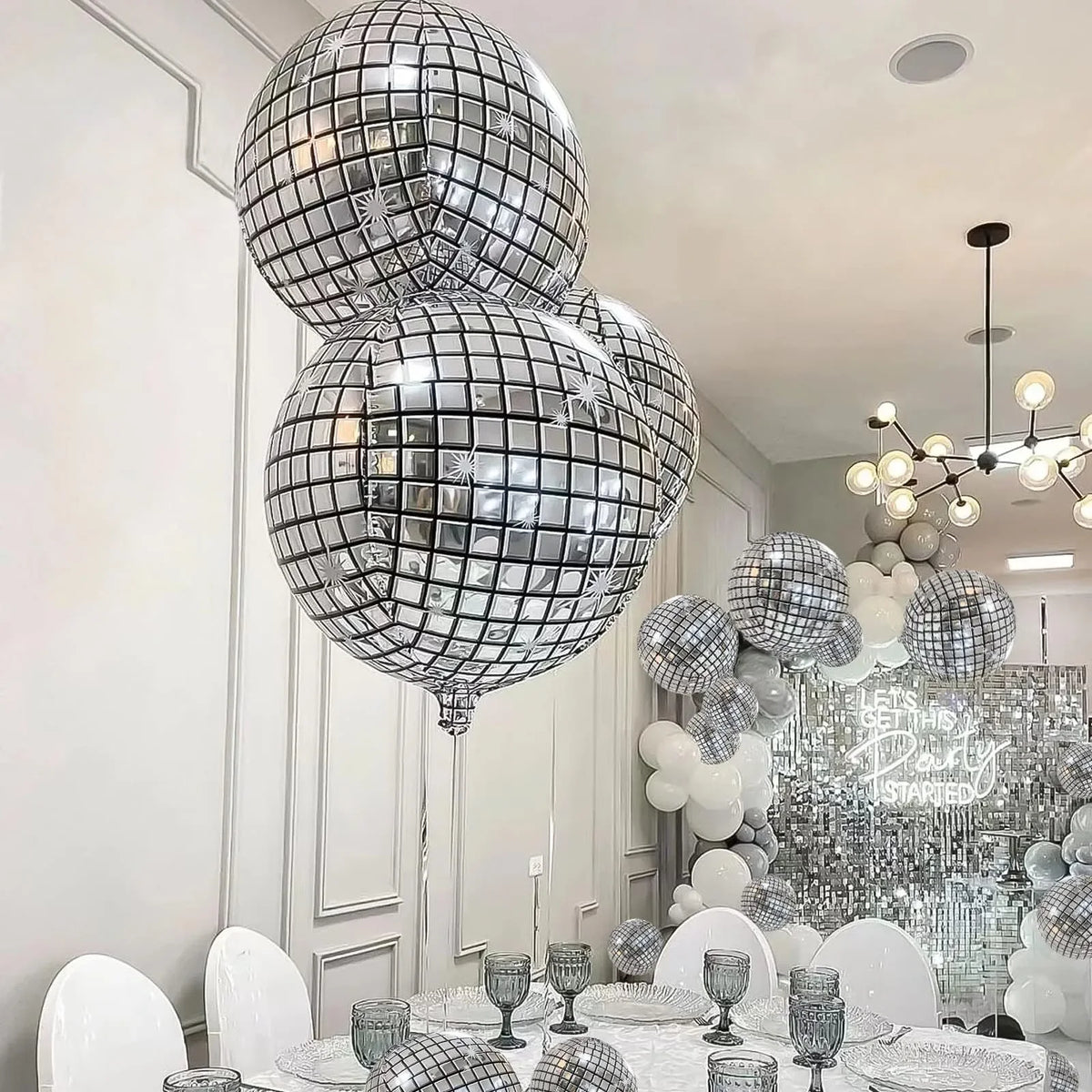 A display of silver disco ball foil balloons in various sizes and a chandelier decoration for a party.