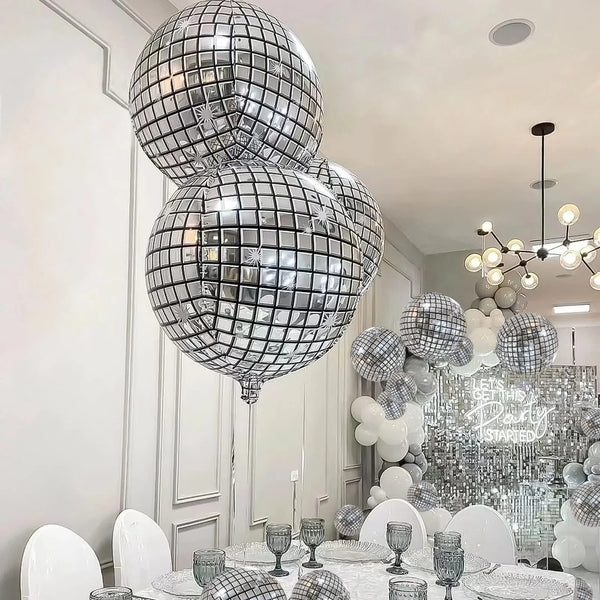 A display of silver disco ball foil balloons in various sizes and a chandelier decoration for a party.