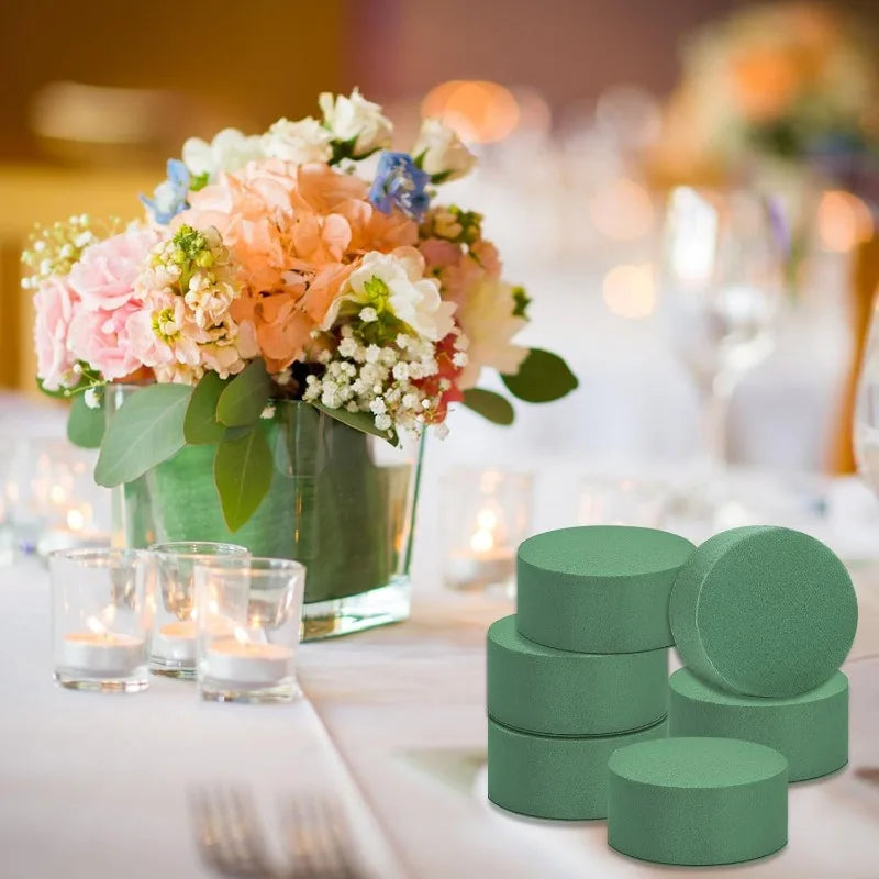 A close-up of round green floral foam blocks displayed on a white table with fresh flowers and candles.