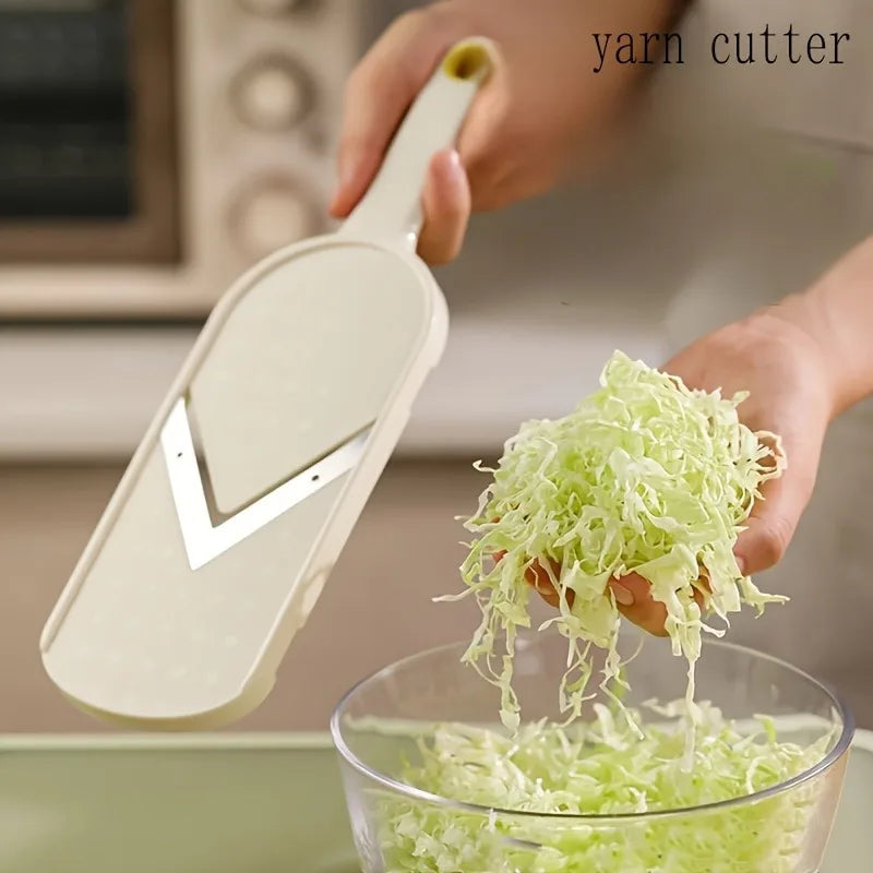 A hand is using a manual yarn cutter to shred cabbage into thin strips in a glass bowl.