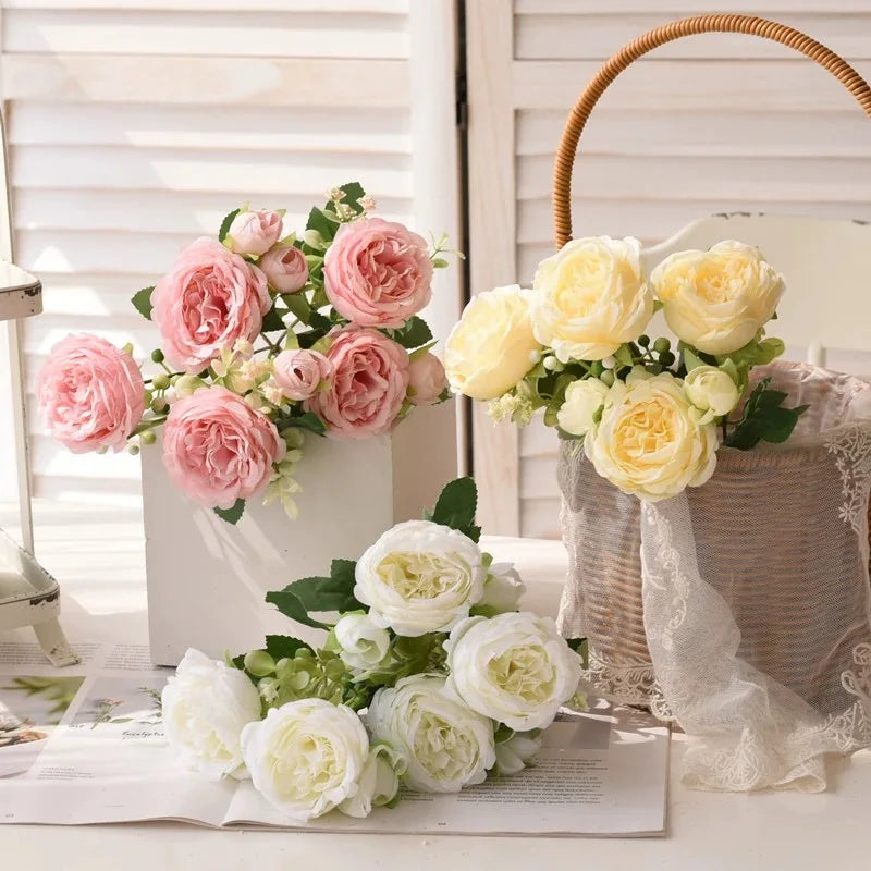 A bouquet of pink and yellow silk peony flowers displayed in a woven basket on a white surface.
