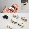 A collection of six white and orange cat figurines used as fridge magnets, displayed on a white surface.