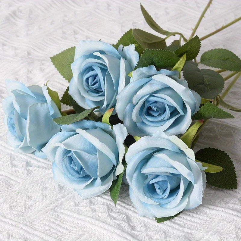 Un ramo de rosas artificiales de seda azul claro con hojas verdes.