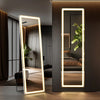 A full-length LED floor mirror with warm light reflecting a modern interior and greenery.