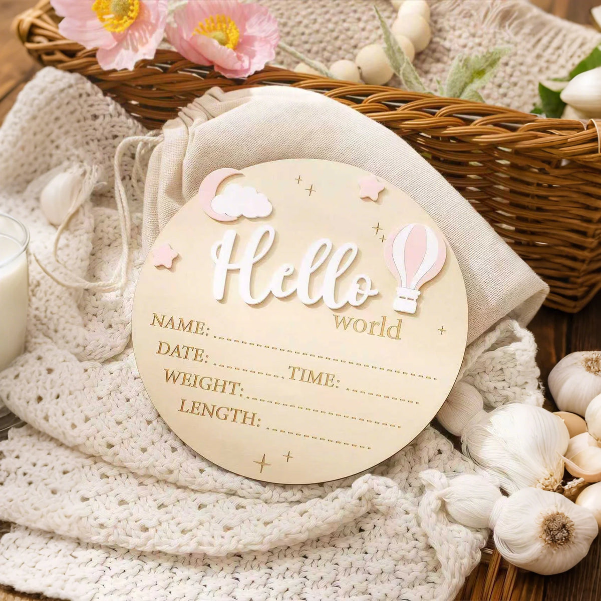 A round wooden birth announcement sign with the word Hello and decorative elements resting on a knitted fabric next to a wick