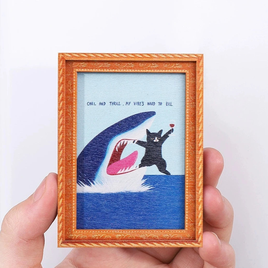 A framed artwork featuring a silhouette of a cat against a blue background with text inside.