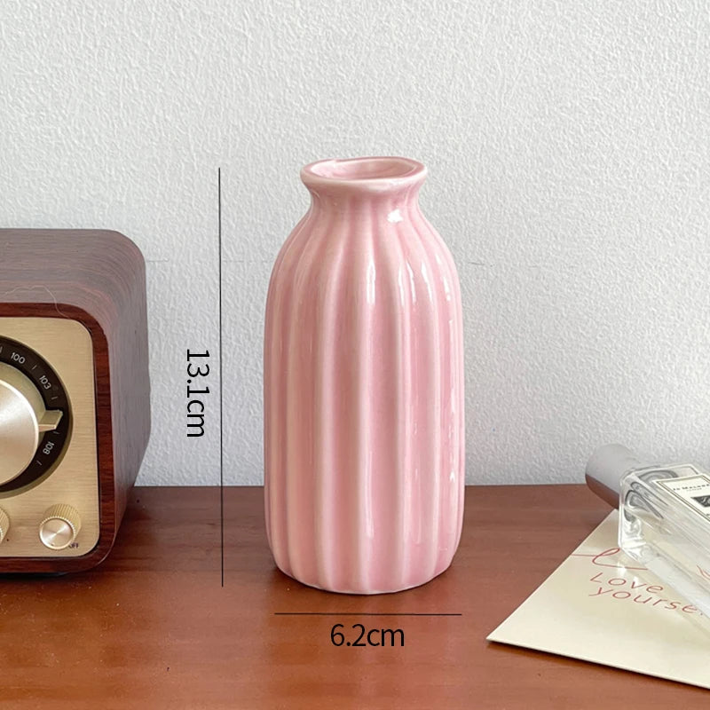 A pink ceramic bud vase with a smooth finish sits on a wooden surface.