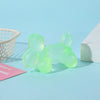 A collection of translucent light green squishy toys arranged on a blue surface next to a white basket and a white box.
