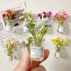 A hand holds a glass jar filled with colorful dried flowers and leaves used for decoration.