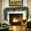 An artificial Norfolk pine garland with warm white lights draped over a fireplace mantel in a rustic living room.