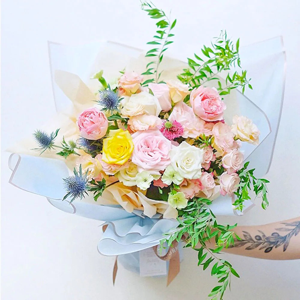 A bouquet of pink and cream roses and greenery wrapped in gold edge floral paper.