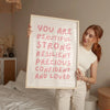 A woman holds a framed canvas print with the text You are beautiful strong resilient precious confident and loved.