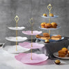 A three-tier gold cake stand with pink and white ceramic plates displaying baked goods.