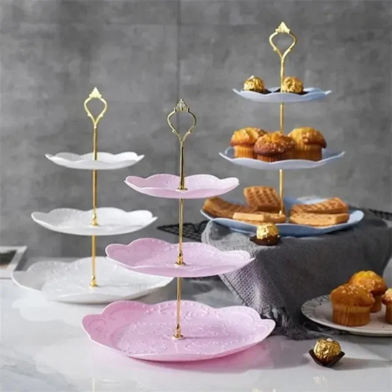 A three-tier gold cake stand with pink and white ceramic plates displaying baked goods.