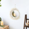 A macrame round wall mirror with a fluffy fringe hanging on a white wall, decorated with greenery and candles.