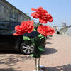 A bouquet of bright red artificial peony flowers displayed in a vase on a paved area.