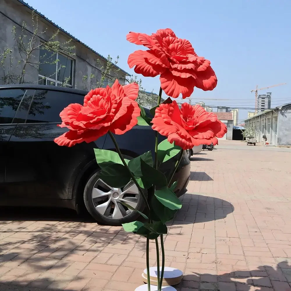 A bouquet of bright red artificial peony flowers displayed in a vase on a paved area.