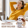 A woman in a yellow sweater is relaxing with her eyes closed while holding a handmade crochet sloth doll and a positive messa