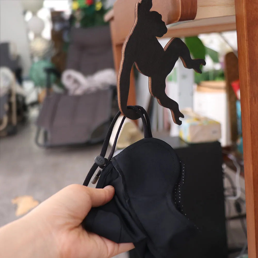 A hand holds a black storage hook shaped like a monkey with a banana design.
