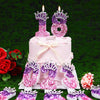 A pink tiered cake decorated with glitter numbers 18 and 25, featuring rhinestone crown toppers and candles.