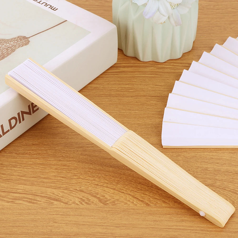 A light wood bamboo folding fan with white paper blades resting on a wooden surface.