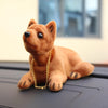 A small, fluffy brown teddy bear dog ornament with gold chain, sitting on a dark surface.