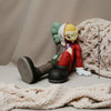 A small, stylized figurine of a bear with green ears and a white face is resting on a beige fabric surface.