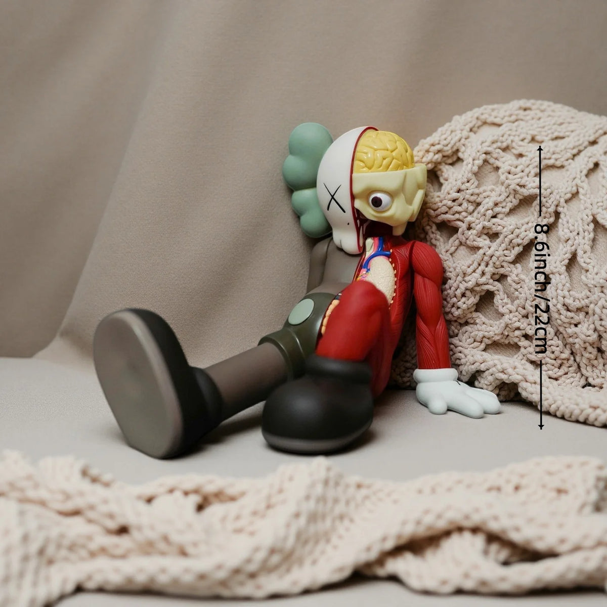 A small, stylized figurine of a bear with green ears and a white face is resting on a beige fabric surface.