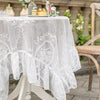 Elegant white floral lace tablecloth covering a wooden table outdoors.