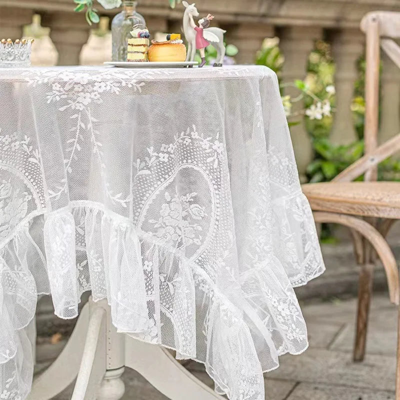 Elegant white floral lace tablecloth covering a wooden table outdoors.