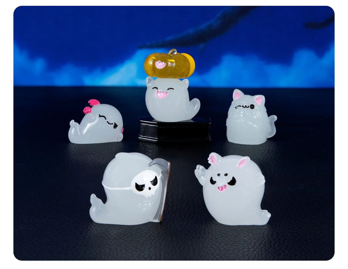 A set of seven white ghost resin ornaments, including a yellow luminous ornament, displayed against a dark blue background.