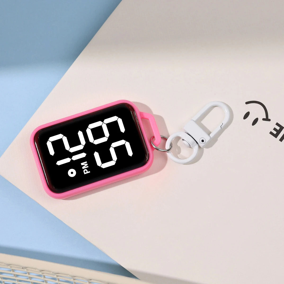 A pink LED keychain pocket watch with a digital display is resting on a white surface.
