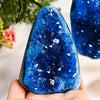 A hand holds a deep blue, faceted crystal cluster with sharp points against a white background.