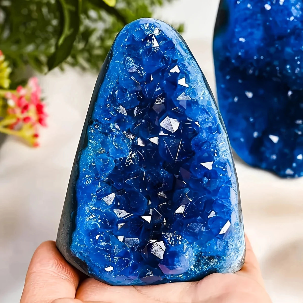 A hand holds a deep blue, faceted crystal cluster with sharp points against a white background.