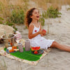 A young girl sits on a sandy beach with a set of five tropical banana leaf coasters and fruit.