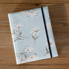 A light blue linen photo album cover featuring a delicate floral pattern and a black stripe.