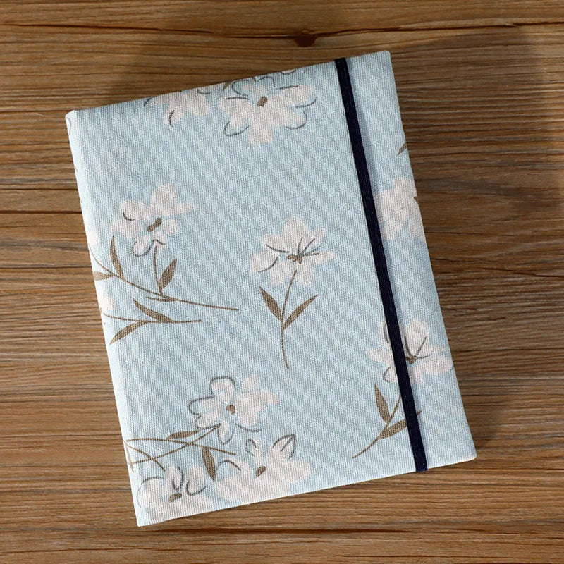 A light blue linen photo album cover featuring a delicate floral pattern and a black stripe.