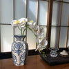 A white porcelain vase holds a spray of white orchids against a light background.