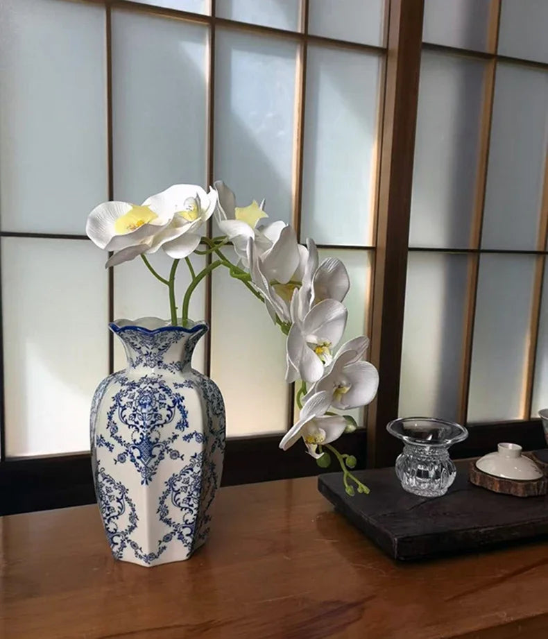 A white porcelain vase holds a spray of white orchids against a light background.