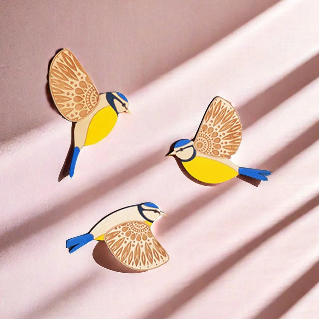 Three vintage wooden bird wall decorations in yellow and blue against a pink background.