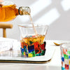 A glass cube filled with amber whiskey is being poured from a bottle onto it.