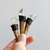 A hand holds three natural crystalHerkimer scepter wands with dark wrappings and clear crystals.