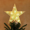 A sparkling, geometric star light fixture is placed on a green pine branch.