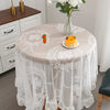 Elegant white floral lace tablecloth covering a round table set with a vase of white flowers.